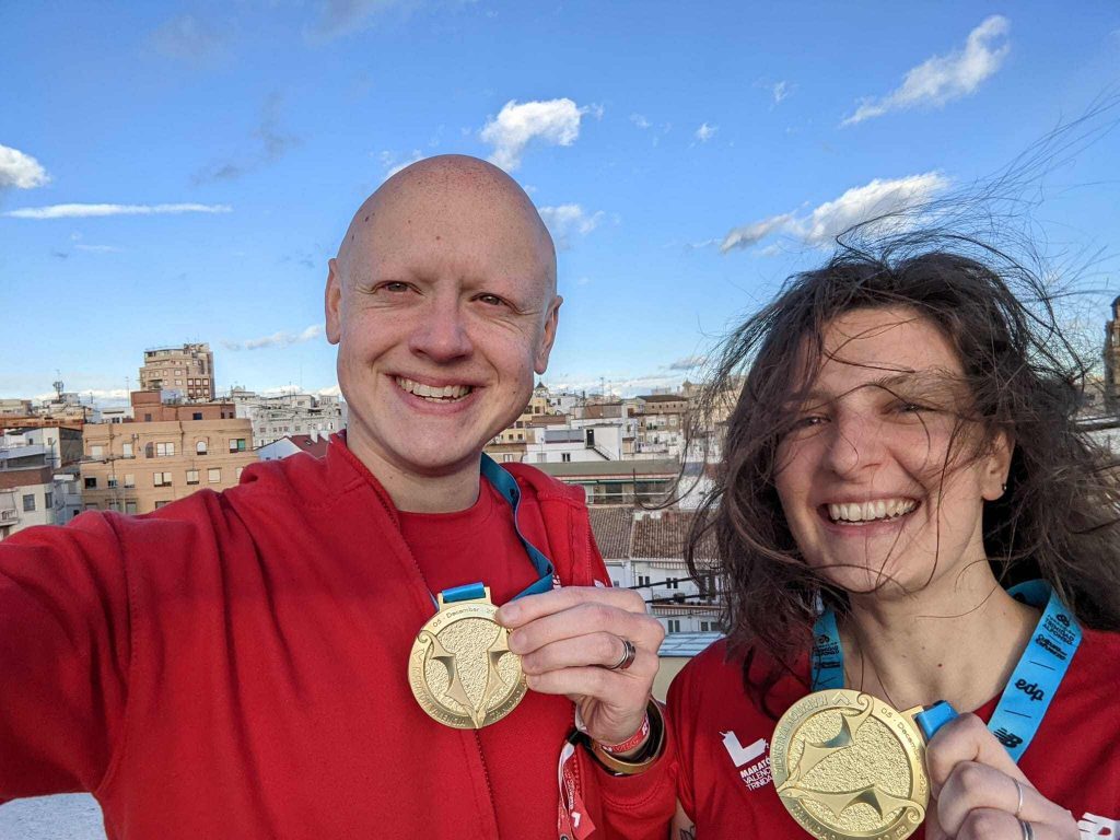 toby and naomi on a windy rooftop in valencia after the marathon, both wearing their medals