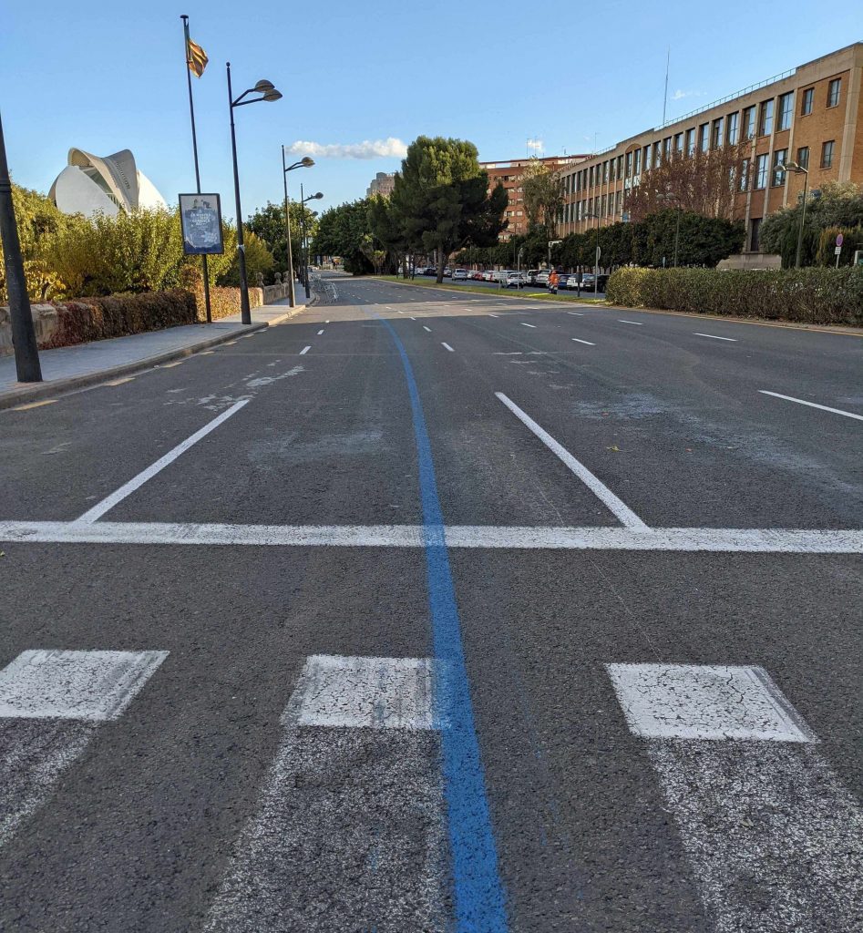 an empty street in Valencia, the road is 4 lanes wide but closed to traffic, there's a blue line painted down the centre of the road.